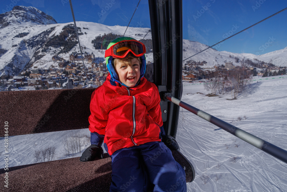Laughing boy in red jacket on ski lift, snowy scenery outside
