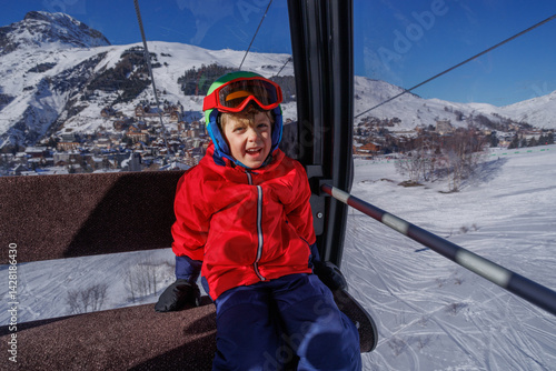 Obraz na płótnie Laughing boy in red jacket on ski lift, snowy scenery outside w salonie