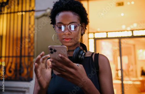 Close-up of young Black woman using smartphone outdoors, focused on screen, possibly managing budget, browsing app store or checking latest social media updates