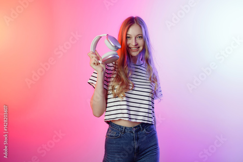 Obraz na płótnie Young woman holding headphones in a colorful background, showcasing a vibrant lifestyle and love for music w salonie