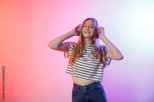 Young woman enjoying music while wearing headphones in a colorful lighting setup
