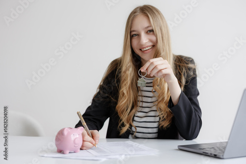 Obraz na płótnie Real estate agent holding house key while finalizing paperwork with savings piggy bank on desk w salonie