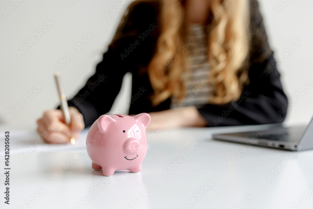 Woman writing notes with piggy bank on desk, illustrating financial planning and budgeting in a modern office