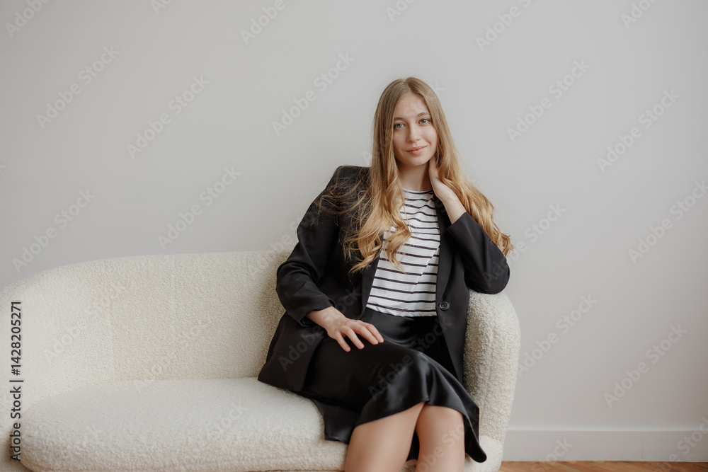 Young professional woman sitting thoughtfully on a cozy couch in a minimalist room during daytime