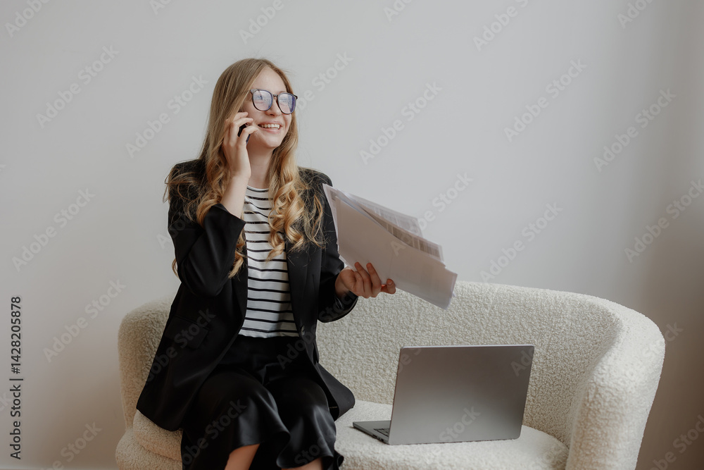 Young professional smiles while talking on the phone and managing documents at a cozy workspace