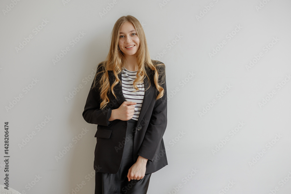 Young woman in professional attire with casual striped shirt poses confidently against a blank wall