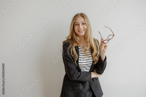 Confident young woman in business attire poses with glasses in office setting