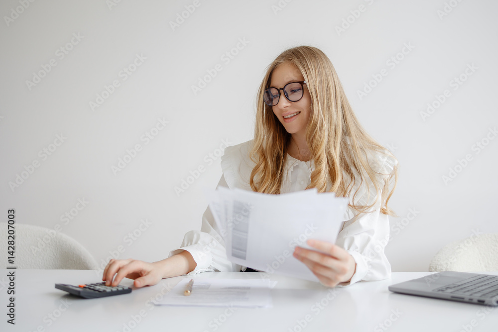 Young woman analyzes financial documents while using calculator in modern office setting during daylight hours