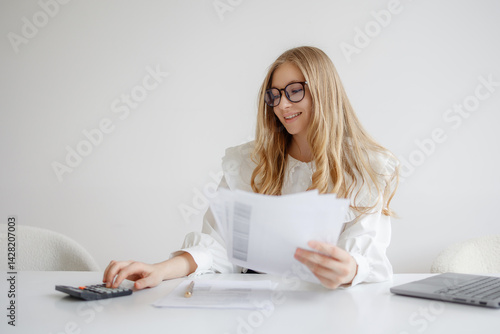 Obraz na płótnie Young woman analyzes financial documents while using calculator in modern office setting during daylight hours w salonie