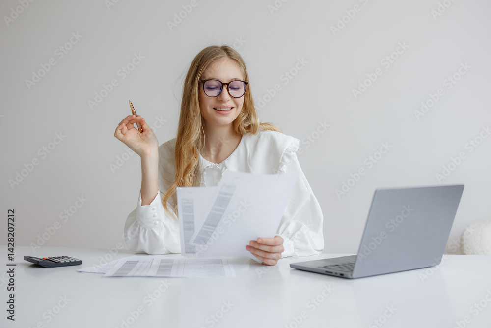 Young woman reviewing documents and planning finances at a modern desk in a bright office space