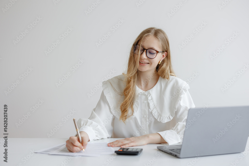 Young woman focused on financial planning while writing at her desk in a minimalist office setting