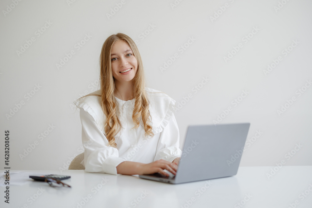Young woman working on a laptop in a bright, minimalistic workspace during daytime