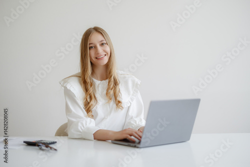 Young woman working on a laptop in a bright, minimalistic workspace during daytime