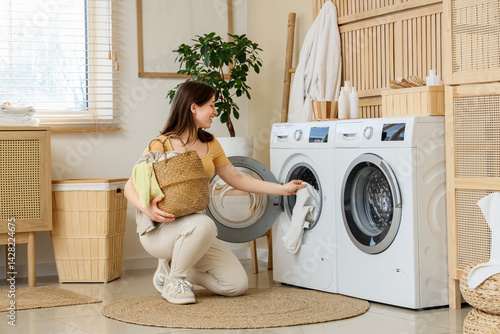 Obraz na płótnie Young woman putting clothes into modern washing machine in laundry room w salonie