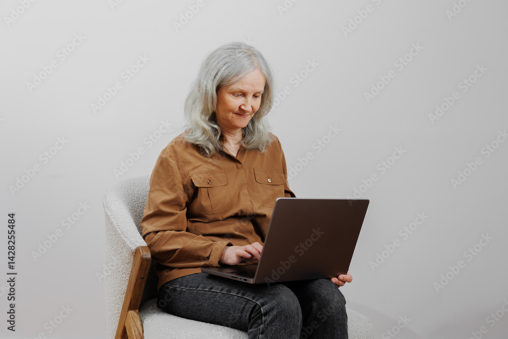 Woman with gray hair sits on chair using laptop in a bright, minimalistic room