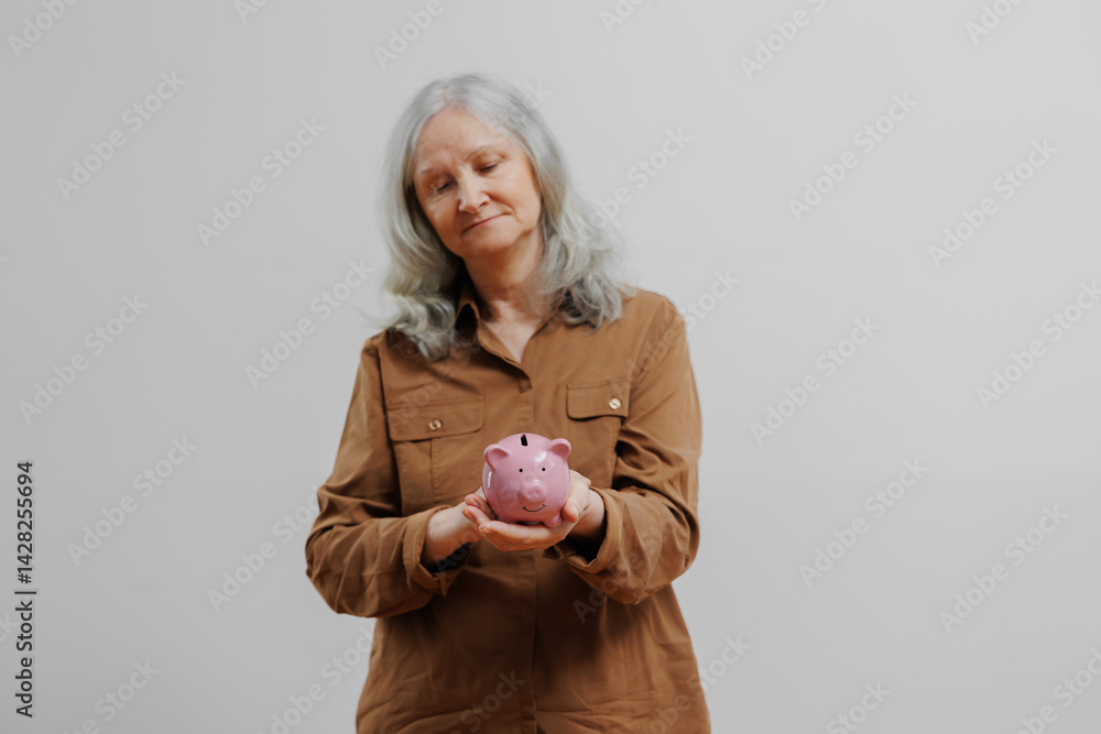 Woman in brown shirt holds a pink piggy bank with a thoughtful expression against a plain background