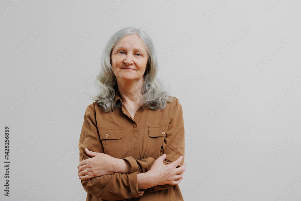 Mature woman with gray hair poses confidently against a plain background, showcasing her relaxed demeanor and warmth