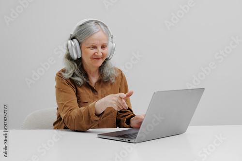 Obraz na płótnie Senior woman wearing headphones engages with laptop in bright, minimalistic space during online activity w salonie