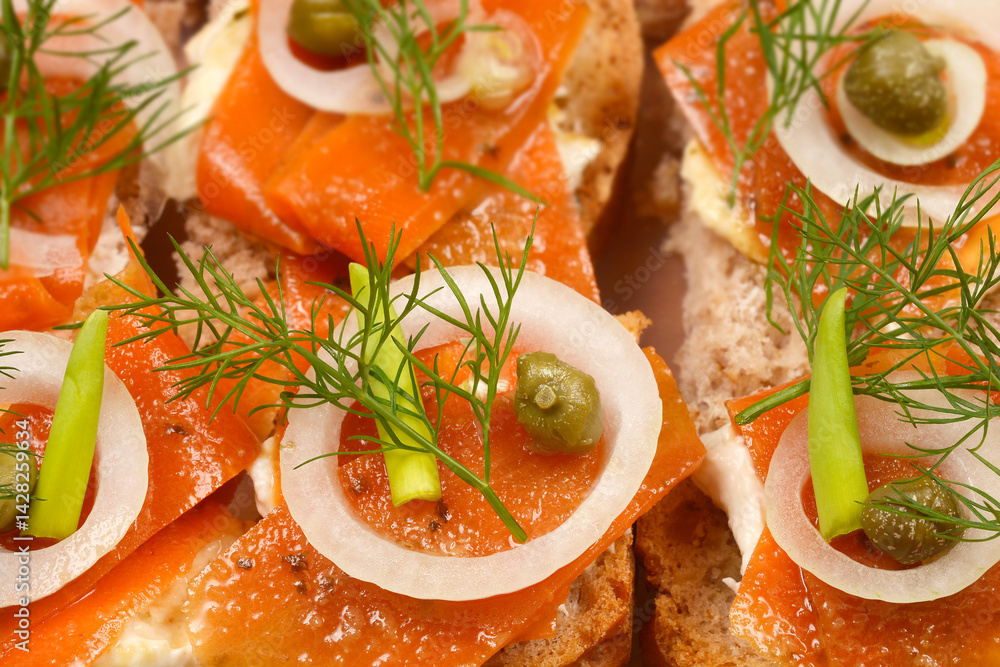 An assortment of open-faced sandwiches featuring carrot slices prepared as vegan salmon, arranged in a clear container