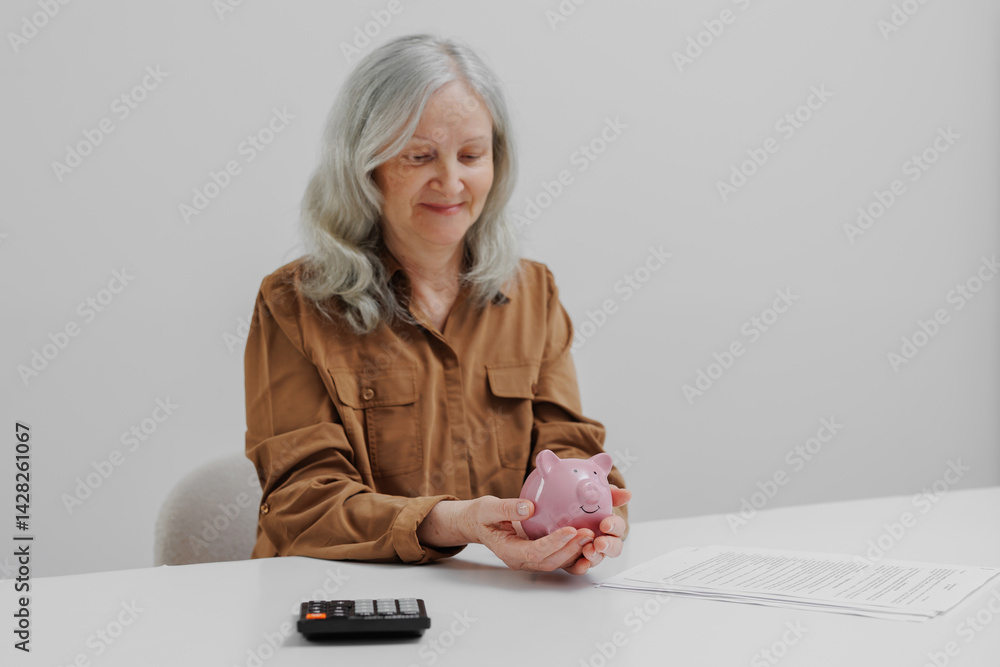 Woman saves money using a pink piggy bank at a white table with documents and a calculator in a well-lit room
