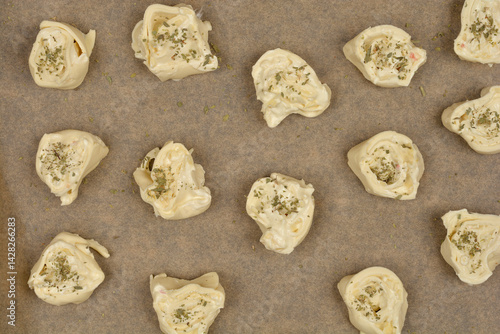 Obraz na płótnie An overhead shot shows raw cheese and oregano puff pastry rolls arranged on parchment paper on a baking sheet, ready to be baked w salonie