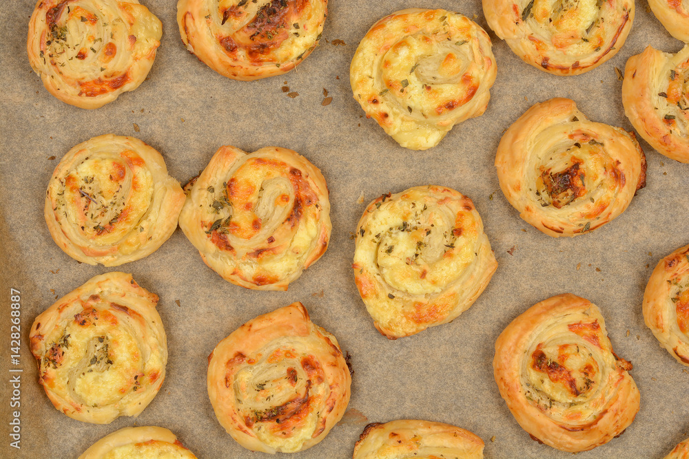 An overhead shot of golden brown cheese puff pastry rolls arranged on parchment paper on a baking sheet