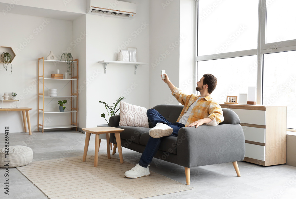 Young man turning on air conditioner from sofa at home