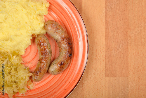 Obraz na płótnie A plate features two grilled homemade sausages served with mashed potatoes and sauerkraut on a light wooden surface w salonie