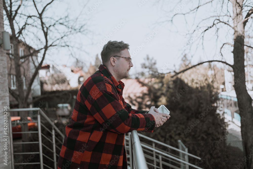 A young blond man wearing glasses, looking at his phone while walking down the street. A modern scene showcasing urban life, technology, and casual street style