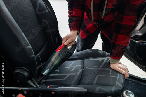 Details of car vacuum cleaning. Professional cropped male worker using wet vacuum cleaner for dirty car interior. Auto car service cleaning the drivers seat, cleaning and vacuuming concept. High