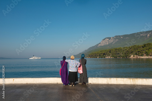 Muslim women visitors to the Turkish seaside town of Akyaka admire the beautiful view and expensive yacht moored in the bay. Turkish coast, Mugla. .