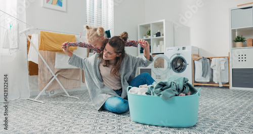 Fotografi A young mother folds laundry while her daughter climbs on her back