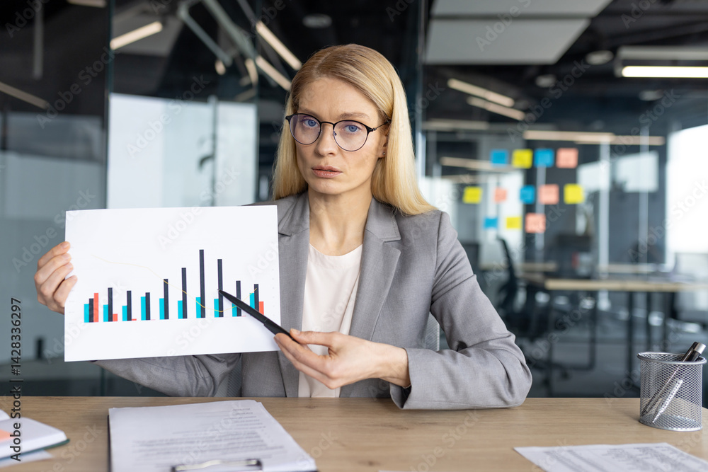 A serious businesswoman presents financial data with a pointer in an office setting, showing a graph. She wears glasses and a suit.