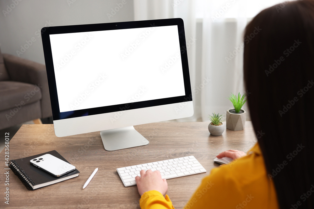 Woman looking at monitor with blank screen at wooden table indoors. Mockup for design