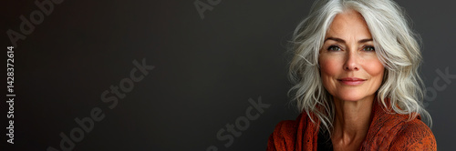 Obraz na płótnie Confident mature woman with wavy silver hair wearing textured orange shawl smiling softly against dark background in studio light Generative AI w salonie