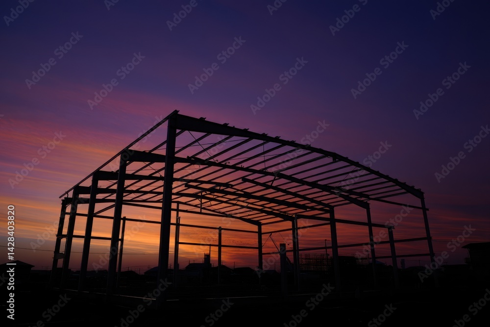 Silhouette of curve metal roof beam and column of large factory building outline structure in construction site against colorful twilight sky background in industrial settlement zone