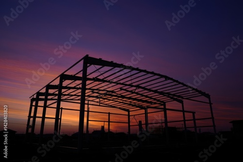 Obraz na płótnie Silhouette of curve metal roof beam and column of large factory building outline structure in construction site against colorful twilight sky background in industrial settlement zone w salonie