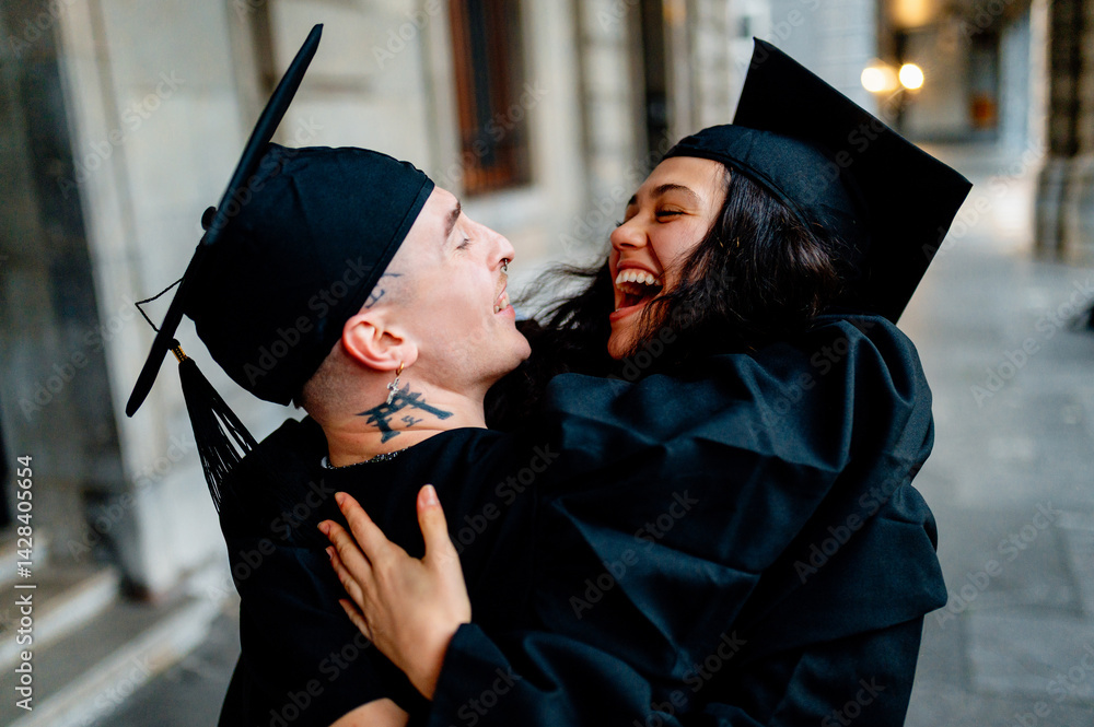 Two young graduates wearing mortarboards and gowns are hugging and laughing joyfully, celebrating their academic achievement