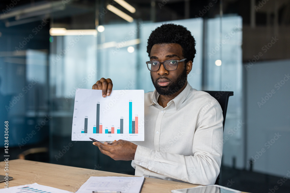 A professional man presents financial data with a graph during a meeting in the office. The analysis is shown with data bars on paper.