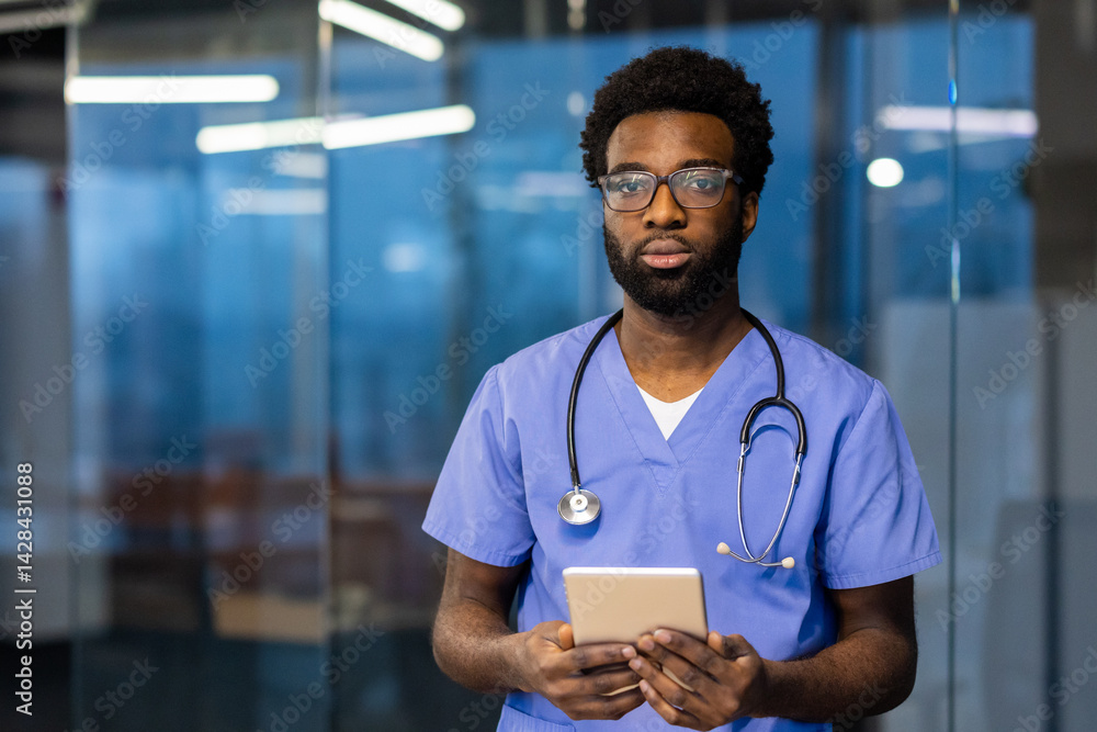 An african american doctor poses confidently with a tablet. He is wearing scrubs and eyeglasses, a stethoscope around his neck.