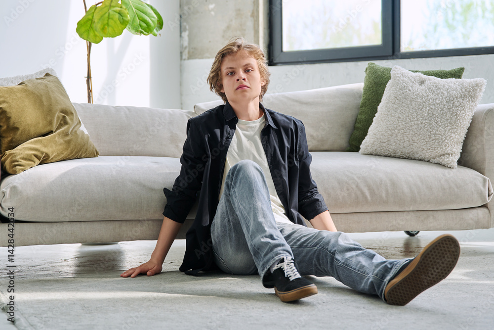 Portrait of handsome relaxed teenage boy sitting on floor near sofa in living room