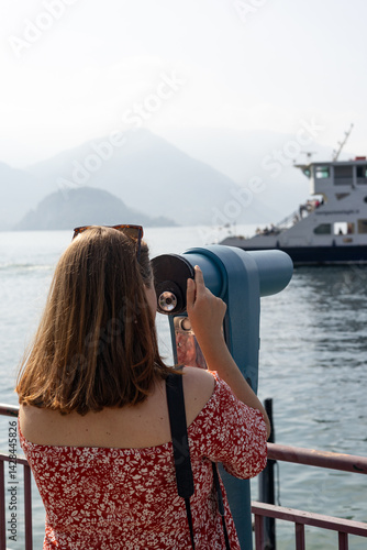 Young 30s woman looking through a coin operated binoculars. Como Lake, Italy.