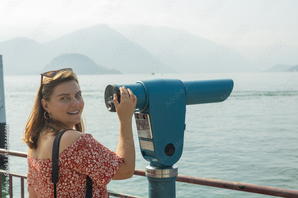 Young 30s woman looking through a coin operated binoculars. Como Lake, Italy.