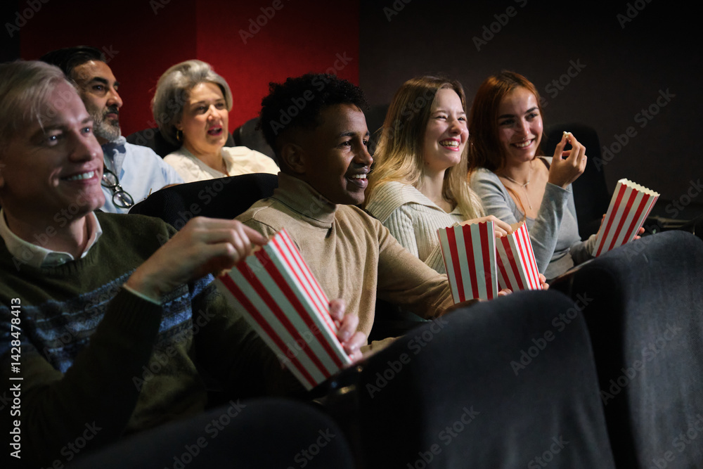 Group of happy multi ethnic friends enjoying film screening and eating popcorn at the movie theater