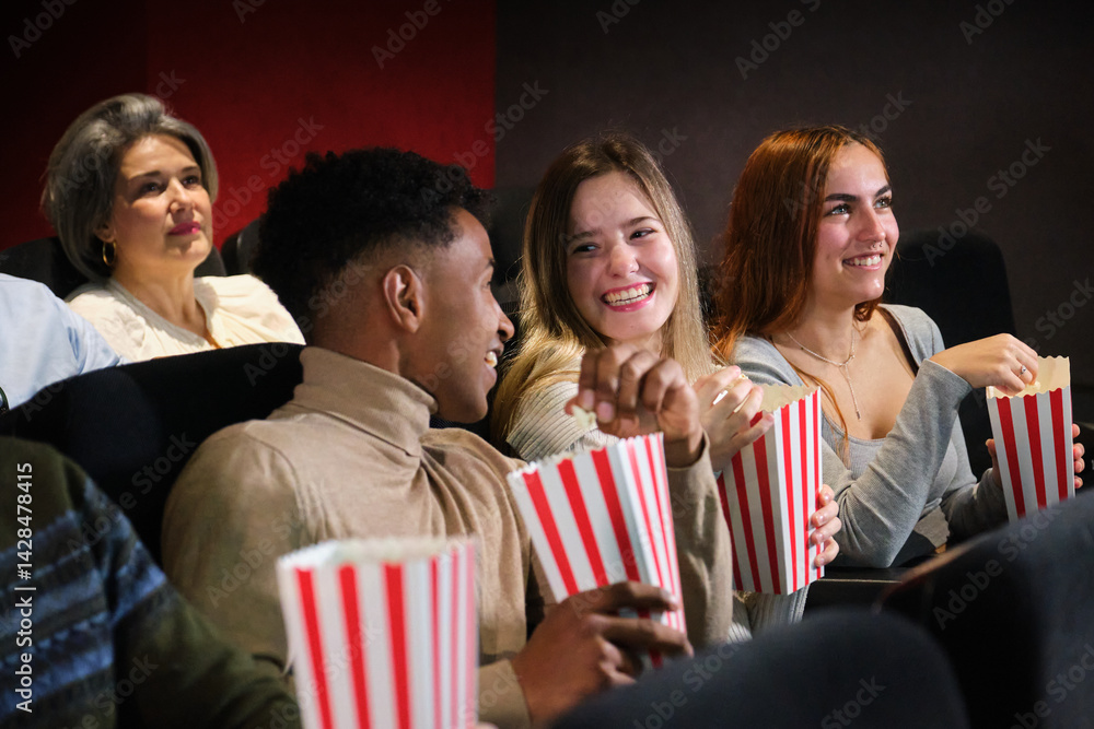 Group of young people watching a movie at the cinema, eating popcorn and having fun