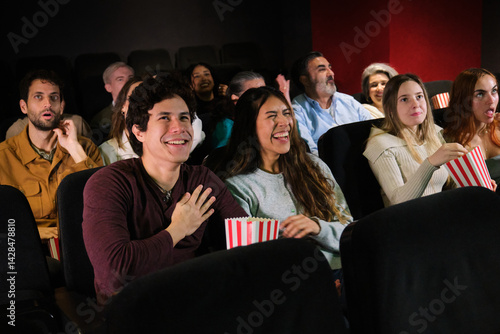 Obraz na płótnie Diverse group of friends having fun watching a comedy movie at the cinema, laughing and eating popcorn w salonie