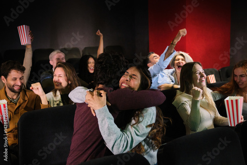 Obraz na płótnie Group of football fans hugging excitedly celebrating their team’s goal while watching the match on the big screen at a cinema w salonie