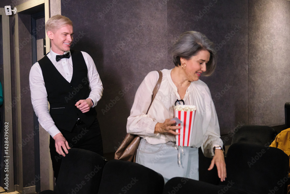Usher helping a woman with popcorn finding her seat in a movie theater