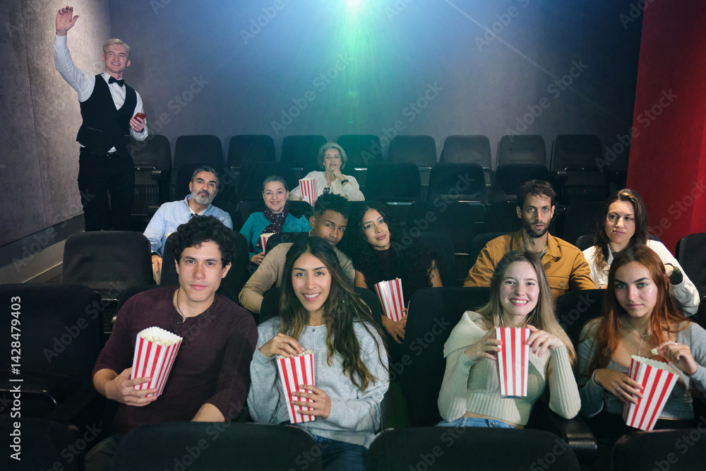 People enjoying film and eating popcorn in movie theater with usher welcoming audience