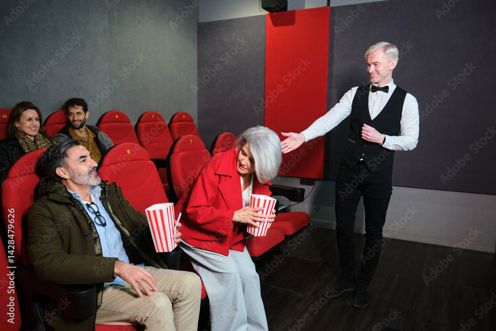 Usher helping senior woman finding her seat in a movie theater, while other people are watching a film